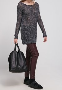 Tjockstickad tröja i mörkgrått, långärmad; åtsittande vinröda läderbyxor; stor svart tote-väska; svarta sandaler med dubbla remmar.