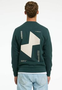 Felpa verde con una finitura testurizzata, caratterizzata da un grande design geometrico color crema sul retro e dettagli testuali bianchi.