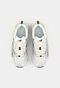 Scarpe da corsa in rete argentate e bianche con superiore texturizzato, suola beige e dettagli neri. Presentano lacci prominenti e logo sulla linguetta.