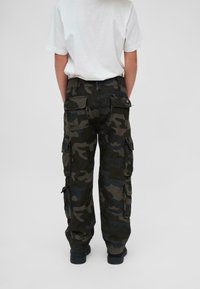 Cargo-byxor i mörk kamouflage, med flera fickor, slitstark tyg och en avslappnad passform. Bärs med en enkel vit T-shirt.