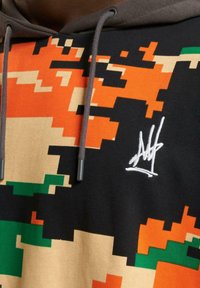 Hooded sweatshirt featuring a pixelated camouflage pattern in orange, green, and black; includes a white embroidered logo and gray drawstrings.
