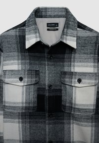 Chemise en flanelle à carreaux gris et noir avec poches poitrine boutonnées, col à pointes et étiquette coupe confort. Texture douce et design structuré.