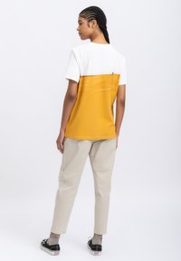 Katoenen T-shirt met een witte bovenhelft en een gele onderhelft, met een zachte textuur, korte mouwen en zichtbare stiksels.