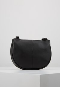 Borsa in pelle nera con forma arrotondata, superficie testurizzata e chiusura con zip. Presenta una tracolla staccabile per maggiore versatilità.