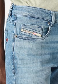 Ljusblå denimjeans med en något blekt finish, som har en bakficketikett och en röd broderad detalj på sidan.