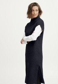 Gestricktes ärmelloses Kleid in dunklem Marineblau mit hohem Kragen und seitlichen Schlitzen. Verfügt über ein strukturiertes Muster und eine darunter geschichtete weiße Bluse.