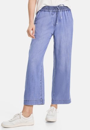 Pantalon large bleu clair avec taille élastique et cordon, porté avec des baskets blanches et un haut blanc.