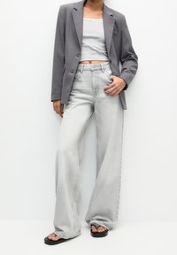 Blazer gris porté sur un crop top gris clair, assorti à un jean en denim clair taille haute, à jambes larges, et des sandales plates noires.