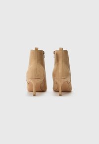 Beige mokkasiner med spiss tå, smal hæl, glidelås og en bakertape for enkel påkledning. Slank tekstur og rent design.