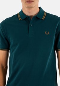 Teal polo shirt van textuur katoen, met een twee-knoopsluiting, contrasterende kraag met gouden strepen en geborduurd logo op de borst.