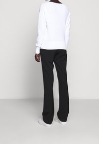 Maglione bianco a maglia con orlo a coste, abbinato a pantaloni neri a gamba larga e sneaker bianche. La vista da dietro mette in evidenza il collo aperto del maglione.