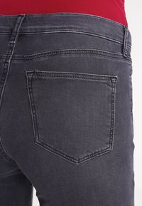 Mörkgrå denimjeans har en enda bakficka med dekorativ sömnad. Tyget ser slätt ut med en något sliten finish.