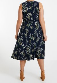 Mörkblå blommig klänning med figurnära midja, utan ärmar och utsvängd kjol. Har vita och gröna blommönster, ihopparad med bruna klackar.