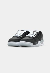 Zapatillas deportivas negras con cordones blancos, un empeine liso y acentos grises. Cuentan con una suela acolchada y una superficie texturizada en el talón.