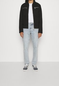 Svart mockajacka med dragkedja i bröstfickorna, vit t-shirt, ljusblå raka jeans och mörka sneakers med vita sulor.