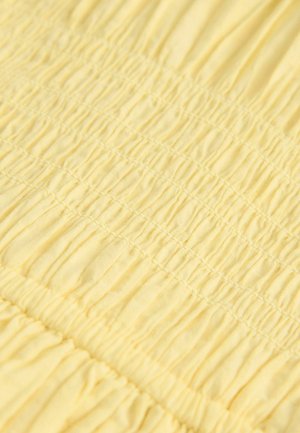 Žltá tkanina s textúrovaným, nielen zhromaždeným vzorom, ktorý má horizontálne záhyby. Mäkký, ľahký materiál s rovnomerne rozmiestneným prešívaním.