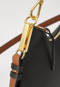 Black leather handbag featuring gold hardware, a detachable strap with brown accents, and a zipper closure detail. Textured surface noted.