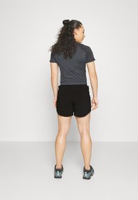 Top desportivo de manga curta, cinza escuro, com mangas raglan, combinado com calções desportivos pretos e ténis de corrida cinza/azuis. Design simples e funcional.