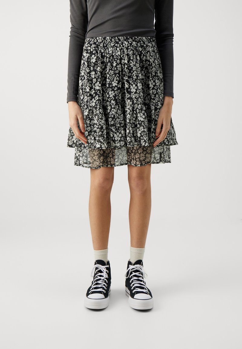 Mustikkakuvioinen kerroshelmahame, jossa on röyhelöhelma ja joustava vyötärö, yhdistetty korkeakantaisiin mustiin tennareihin ja beigeihin sukkiin.