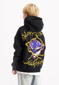 Zwarte hoodie met een grote graphic van een gezicht omringd door gele bliksemschichten op de achterkant. Heeft een ruime capuchon en ribgebreide manchetten.