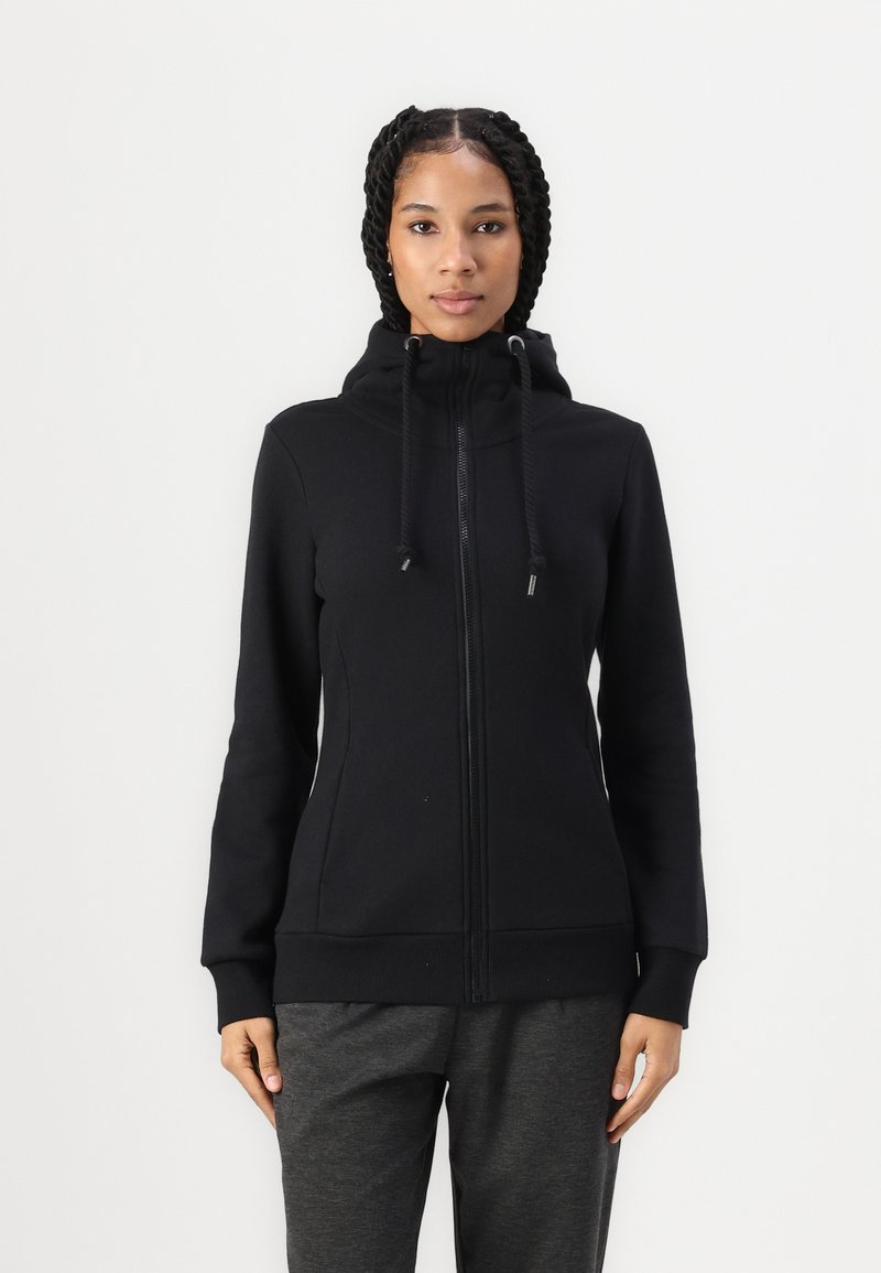 Haut de sweatshirt zippé noir avec col montant, accents de cordon de serrage et manches longues. Texture douce et design ajusté, associé à un pantalon gris.