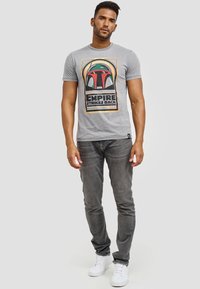 Grå bomulds T-shirt med et livligt grafisk motiv af en hjelm og teksten "Empire Strikes Back." Sammen med grå jeans og hvide sneakers.