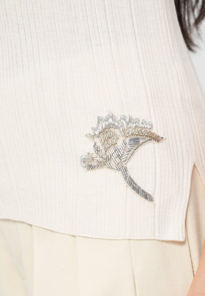 Ribbed cream-sävytetty neulepaita, jossa on hopeansävyistä kukkaembroidery tietty reunoilla, valmistettu pehmeästä materiaalista, jossa on kevyet sivuhalkeamat.