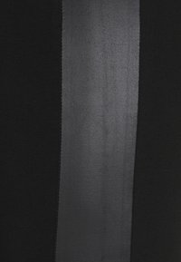 Černá tkanina s lesklým černým svislým pruhem. Textura je na pruhu hladká a na okolní látce mírně jemně proužkovaná.