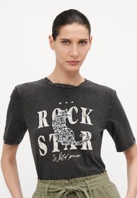 Juodas medvilnės marškinėliai su blizgučiais dekoruota katės dizainu ir tekstu "ROCK STAR" ryškiomis baltomis raidėmis. Trumpi rankoviai ir laisvas kirpimas.