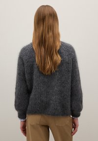 Maglione grigio e morbido con vestibilità ampia e spalle scese, caratterizzato da polsini e bordo a costine, abbinato a pantaloni color cammello.