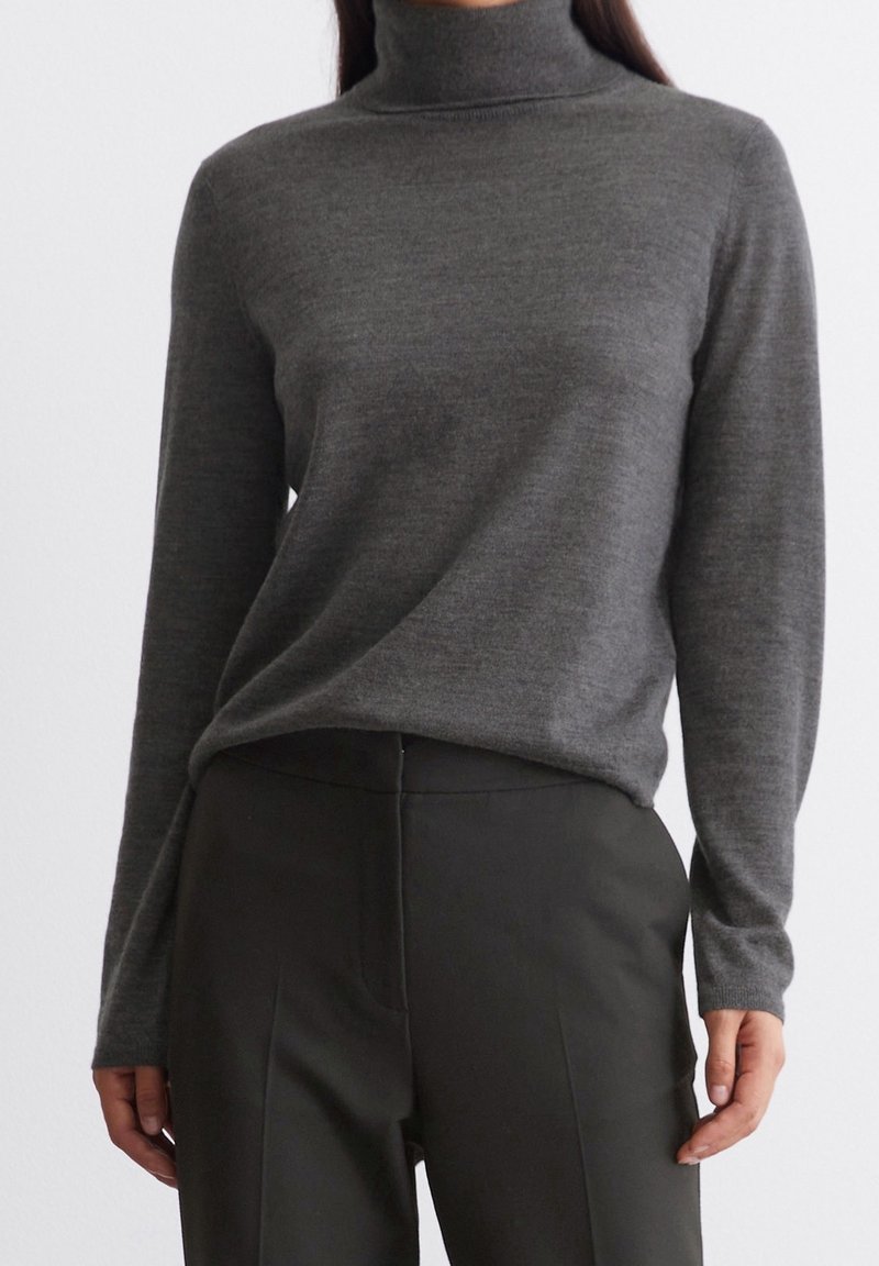 Un pull à col roulé gris en maille douce, doté de manches longues et d'une coupe décontractée. Associé à un pantalon sombre. Texture lisse.