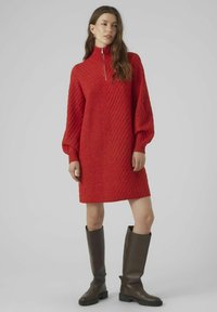 Abito rosso a maglia con motivo diagonale testurizzato, colletto alto, cerniera argentata e maniche a sbuffo, abbinato a stivali marroni al ginocchio.