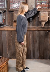 Jonge vrouw past ouderwetse elektrische schakelaars aan in een rustieke houten kamer, gekleed in een grijze top en broek met luipaardprint.