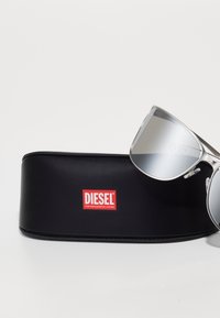 Srebrne sončne naočare v črni usnjeni etui z rdečim logotipom DIESEL. Sončne naočare imajo eleganten dizajn s prozornimi okvirji.