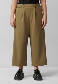 Pantalons larges marron avec des plis et des accents de boutons à la taille ; associés à des chaussures à plateforme noires et épaisses. Texture de tissu lisse.