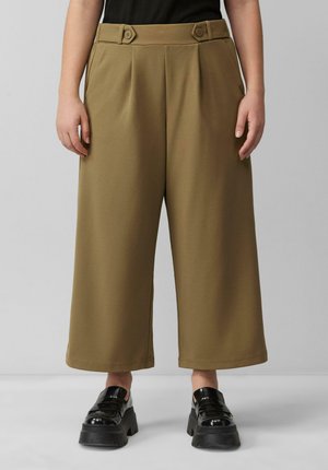 Pantalons larges marron avec des plis et des accents de boutons à la taille ; associés à des chaussures à plateforme noires et épaisses. Texture de tissu lisse.
