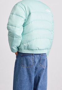 Ljus mintgrön pufferjacka med ett kviltat mönster, elastisk midja och en logga vid axeln, kombinerad med luftiga blå denimjeans.