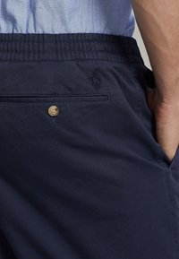 Marina blå shorts i mjukt tyg, med elastisk midja, knappstängning och en bakficka med en subtil logotyp sydd.