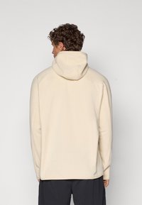 Cream hooded sweatshirt with a soft texture, featuring a relaxed fit and dropped shoulder seams, shown from the back.