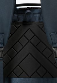 Panneau texturé noir avec motif géométrique ; comporte des sangles et des accessoires navy ; design structuré adapté aux sacs à dos.