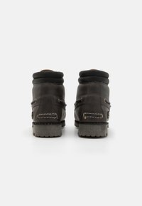 Bruine leren enkelboots met een gevoerde zwarte kraag, stevige grijze zool en gestikte accenten. Het ontwerp heeft een ronde neus en vetersluiting.