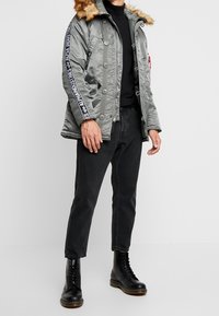 Grön metallisk jacka med fuskpälsdetalj, knapp- och dragkedjestängning, sidofickor och svarta ärmar med vit logotext. Matchad med svarta jeans och stövlar.