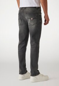 Jeans de mezclilla gris oscuro con un corte slim, diseño de cinco bolsillos, un ligero desgastado y una pequeña etiqueta de logo en el bolsillo trasero. Combinados con zapatillas blancas.