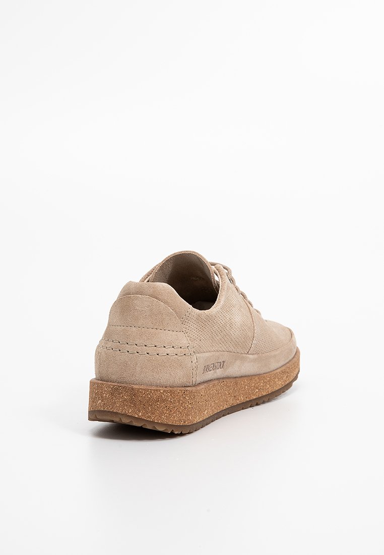 Beige suède sportschoenen met een gestructureerde bovenkant en een gladde vetersluiting. Kurkzool biedt lichte demping. Subtiele stikdetails aan de zijkanten.