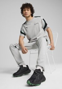 Harmaa urheiluva outfit, jossa on lyhythihainen paita mustilla yksityiskohdilla, yhdistettynä samanvärisiin housuihin; mustat tennarit, joissa on vihreät pohjat.