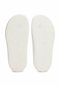 Suelas de goma blanca con superficie texturizada, con el nombre de la marca impreso en letras en relieve y patrones de agarre en forma de círculo.