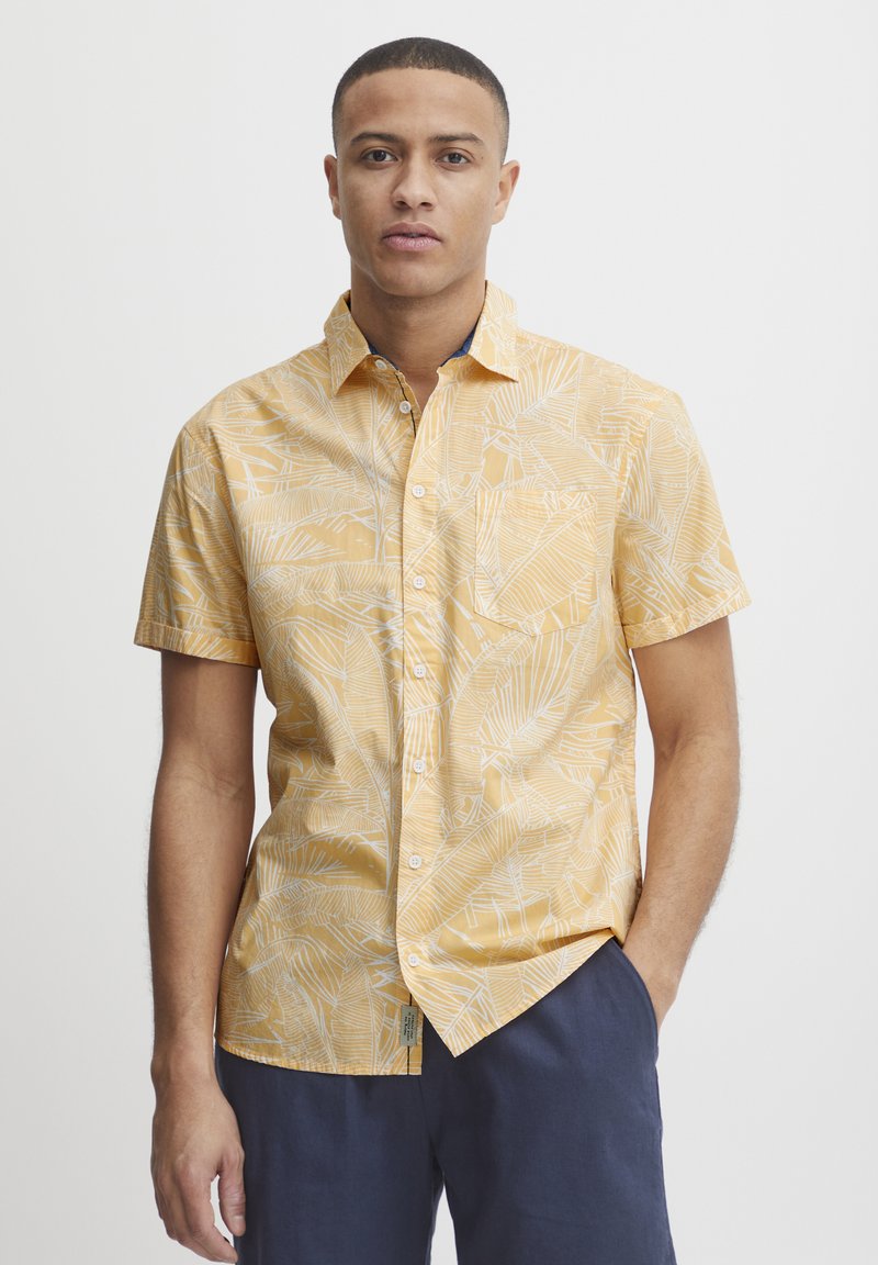Korte mouwen shirt gemaakt van lichtgewicht stof, geel met een wit bladrand patroon, met knoopsluiting aan de voorkant, puntkraag en borstzakdetail.