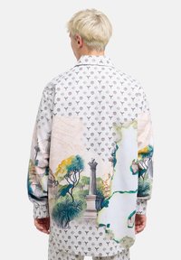 Lange mouwen shirt met een witte basis, met een kleurrijke tuin scène en lichte patronen doorheen. Glad stof, ontspannen pasvorm.