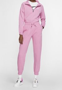 Rosa Nike träningsdräkt med dragkedja i kragen, med en logotyp på bröstet och dragsko i midjan. Kombinerad med vita sneakers och randiga strumpor.