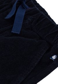 Pantaloni in corduroy blu navy con una consistenza morbida, dotati di un laccio frontale e di un piccolo etichetta logo in vita.